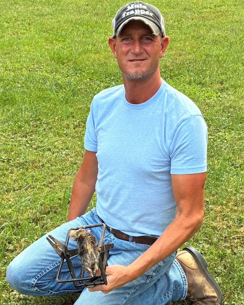 Adam Scott of The Trapper Wildlife Removal kneeling in a north central Indiana yard holding a mole trap